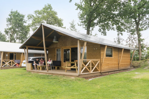 Famiglia rilassata davanti a una tenda safari in legno a Kampeerdorp de Zandstuve, Paesi Bassi.