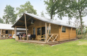 Familie entspannt vor einem Safari-Zelt aus Holz im Kampeerdorp de Zandstuve in den Niederlanden.