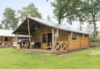 Famiglia rilassata davanti a una tenda safari in legno a Kampeerdorp de Zandstuve, Paesi Bassi.