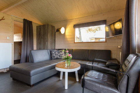 Sala de estar dentro de una tienda safari Rheezerlodge en Kampeerdorp de Zandstuve, Países Bajos, con sofá y TV.