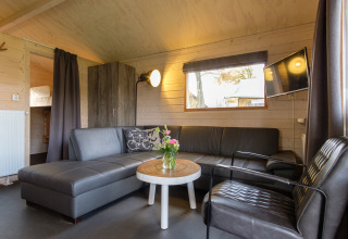 Sala de estar dentro de una tienda safari Rheezerlodge en Kampeerdorp de Zandstuve, Países Bajos, con sofá y TV.