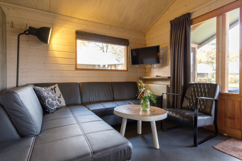 Modern living area inside Rheezerlodge safari tent at Kampeerdorp de Zandstuve, Netherlands, with sofa and TV.
