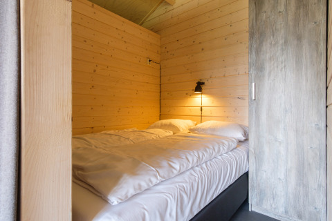 Cozy bed with white linens inside a safari tent at Rheezerlodge, Kampeerdorp de Zandstuve, Netherlands.