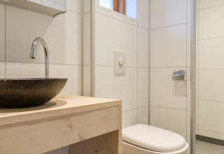 Baño moderno con inodoro suspendido, lavabo redondo y mueble de madera en una tienda safari en Rheezerlodge.