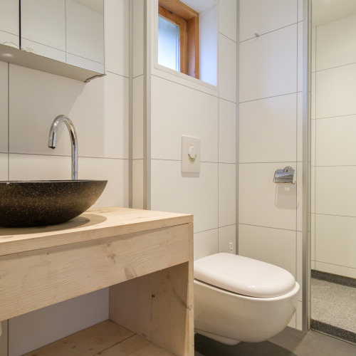 Baño moderno con inodoro suspendido, lavabo redondo y mueble de madera en una tienda safari en Rheezerlodge.