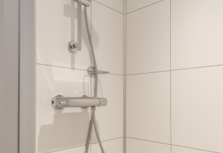 Moderne douche met verstelbare douchekop en witte tegels in Rheezerlodge, Kampeerdorp de Zandstuve, Nederland.