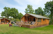 Photo extérieure de la Rheezerlodge DeLuxe high à Kampeerdorp de Zandstuve, Pays-Bas, avec vélos et lodges.
