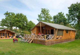 Außenaufnahme von Rheezerlodge DeLuxe high im Kampeerdorp de Zandstuve, Niederlande, mit Fahrrädern und Hütten.