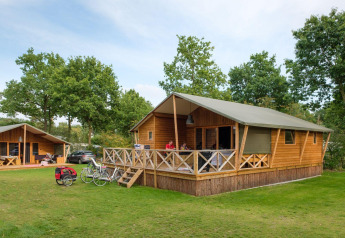 Photo extérieure de la Rheezerlodge DeLuxe high à Kampeerdorp de Zandstuve, Pays-Bas, avec vélos et lodges.