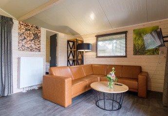 Salon de lodge moderne avec canapé d’angle marron, table basse, œuvres murales, lampe et TV fixée.