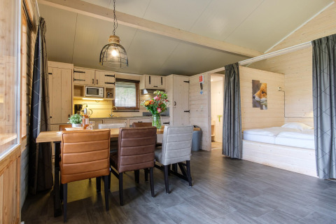 Interior of a Rheezerlodge DeLuxe high at Kampeerdorp de Zandstuve, showing dining table, bed, and kitchen.