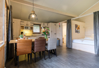 Intérieur d'une Rheezerlodge DeLuxe high à Kampeerdorp de Zandstuve montrant table, lit et cuisine.