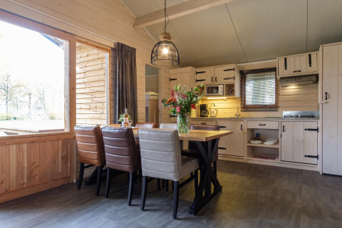 Acogedora cabaña con comedor moderno, cocina abierta de madera clara y grandes ventanas al exterior.
