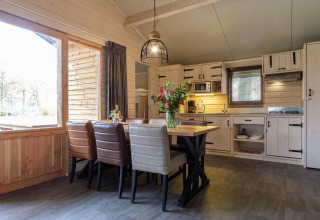 Acogedora cabaña con comedor moderno, cocina abierta de madera clara y grandes ventanas al exterior.