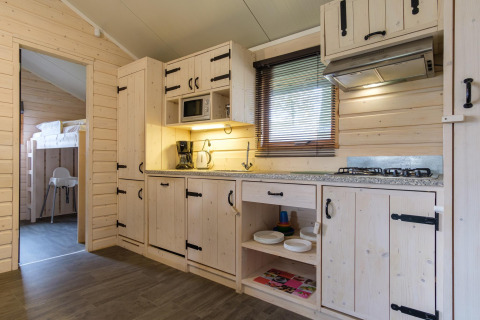 Cocina de cabaña moderna con revestimiento de madera clara, electrodomésticos, estufa y vista a literas.