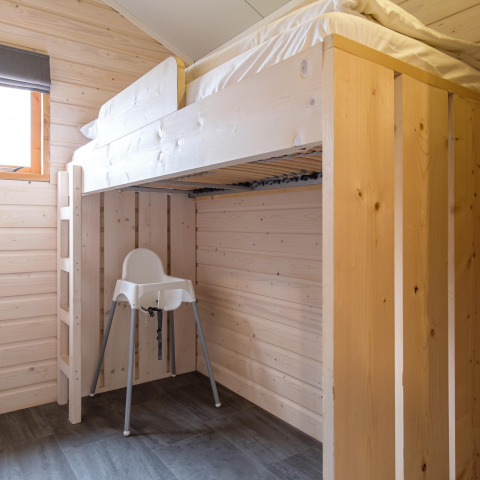 Modernes Zimmer in einer Lodge mit einem Hochbett aus hellem Holz und einem weißen Hochstuhl darunter.