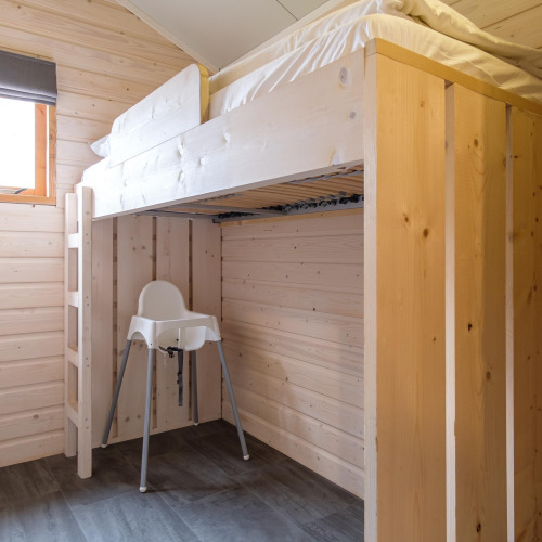 Habitación moderna en un lodge con litera de madera clara y una trona blanca colocada debajo de la cama.