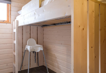 Modernes Zimmer in einer Lodge mit einem Hochbett aus hellem Holz und einem weißen Hochstuhl darunter.