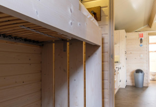 Interieur van een lodge met licht houten panelen, stapelbed en zicht op badkamer met vuilnisbak.