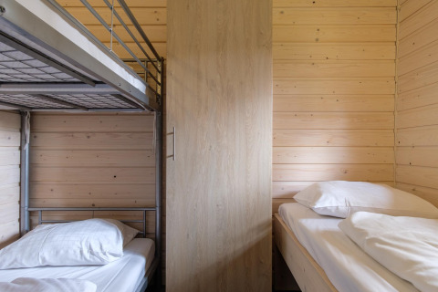 Sfeervolle lodgekamer met stapelbed, enkel bed, houten wanden en een kleerkast in het midden.