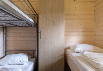 Intérieur d’une chambre de lodge avec lits superposés, lit simple, murs boisés et armoire au centre.