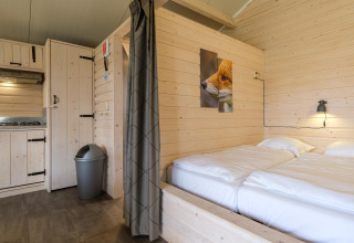 Gezellig lodge-interieur met lichte houten muren, tweepersoonsbed, kleine keuken en een vosfoto aan de muur.