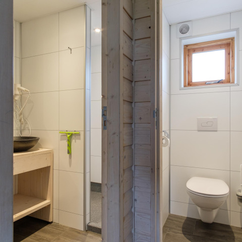 Moderne lodgebadeværelse med hvidt flisegulv, håndvask, hårtørrer og separat toilet med vindue.