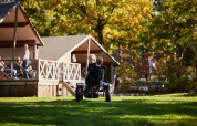 Deux enfants font du kart autour de lodges en bois entourés d’arbres et de verdure en plein air.