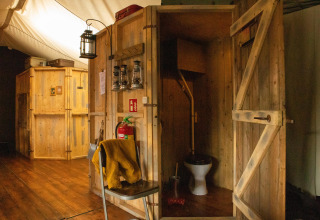 Rustic wooden cabin interior with vintage-style toilet and lanterns at Feather Down Hoeve de Betuwe holiday park.