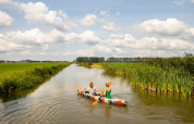 Dos personas reman en un colorido kayak por un canal tranquilo rodeado de campos verdes en Gelderland, Países Bajos.
