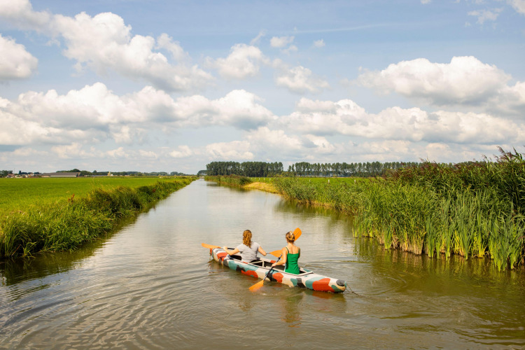 Dos personas reman en un colorido kayak por un canal tranquilo rodeado de campos verdes en Gelderland, Países Bajos.