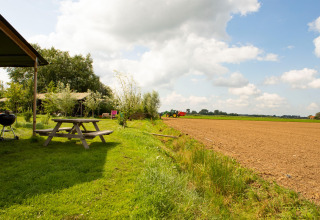 Holiday park scene in Gelderland, Netherlands with picnic table, grill, green grass and a distant tractor.
