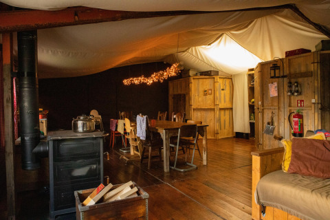 Acogedor interior de cabaña de madera con mesa de comedor, estufa y luces en parque vacacional holandés