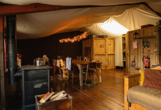 Gezellige houten hutinterieur met eettafel, houtkachel en sfeerverlichting in een Nederlands vakantiepark