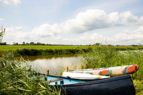 Deux bateaux reposent dans l’herbe haute près d’un canal à Dreumel, Gueldre, Pays-Bas, sous un ciel nuageux.