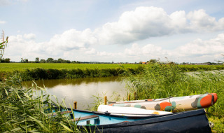 Dos botes descansan entre hierba alta junto a un canal cerca de Dreumel, Gelderland, Países Bajos, bajo cielo nublado.