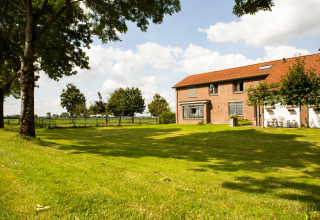 Großer Garten mit grüner Wiese und Bäumen vor einem Haus im Feather Down Hoeve de Betuwe Ferienpark.