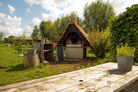 Outdoor pizza oven with a wooden roof and garden scenery at Feather Down Hoeve de Betuwe holiday park.