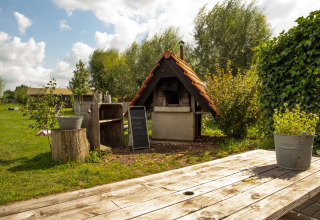 Outdoor pizza oven with a wooden roof and garden scenery at Feather Down Hoeve de Betuwe holiday park.