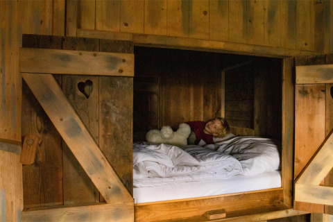 Un niño descansa con un peluche en una acogedora cama de madera en Feather Down Hoeve de Betuwe, Gelderland.