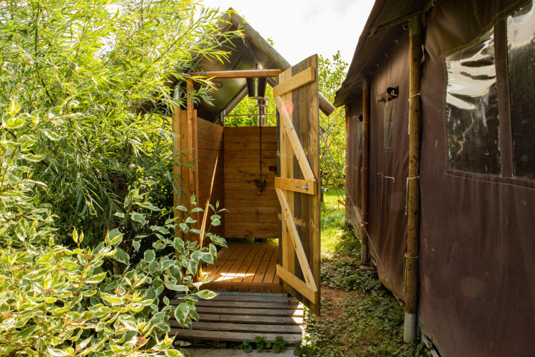 Ducha exterior junto a una tienda de campaña rodeada de vegetación en Feather Down Hoeve de Betuwe, Holanda.