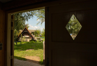 Uitzicht door een open deur op een zonnige tuin met picknicktafel en huisje in Gelderland, Nederland.