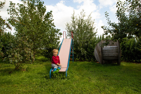 Bambino seduto su uno scivolo nel giardino verde di Feather Down Hoeve de Betuwe in Gelderland, Paesi Bassi.
