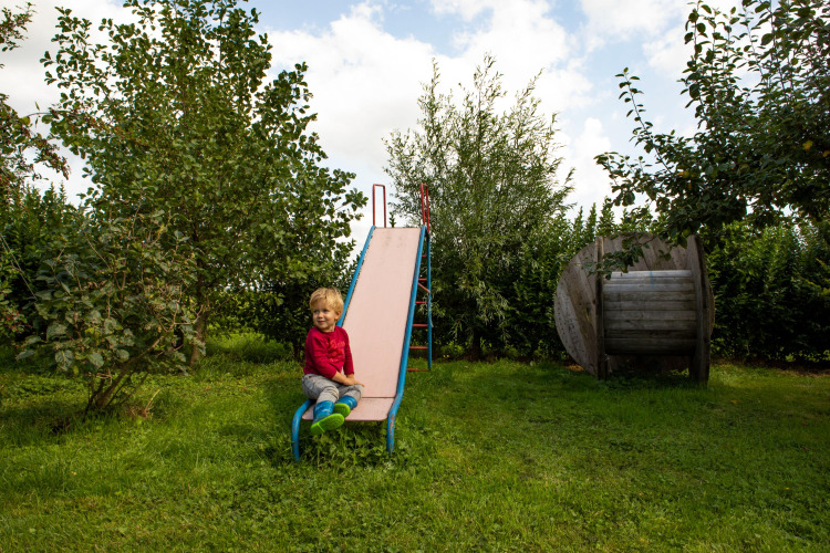 Child sitting on a slide in the green garden of Feather Down Hoeve de Betuwe holiday park in Gelderland.