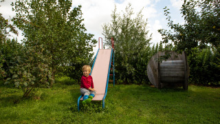 Niño sentado en un tobogán en el jardín verde del parque vacacional Feather Down Hoeve de Betuwe en Gelderland.