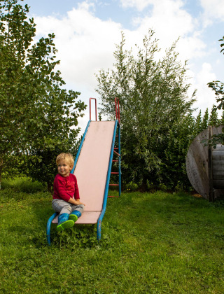 Niño sentado en un tobogán en el jardín verde del parque vacacional Feather Down Hoeve de Betuwe en Gelderland.