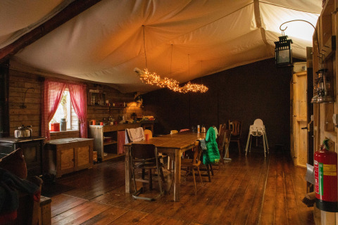 Gemütliches Hüttenzimmer mit Holzinterieur, rustikalem Esstisch, Lichterkette und offener Küche.