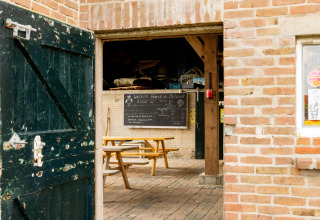 Offene Scheunentür mit Picknicktischen und einer Tafel bei Feather Down Hoeve de Betuwe in Gelderland, Niederlande.