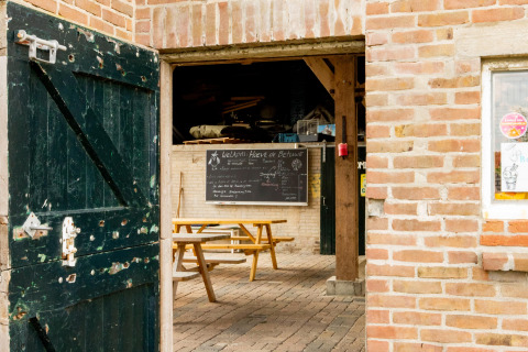 Porta di una stalla aperta verso tavoli da picnic e lavagna a Feather Down Hoeve de Betuwe, Gelderland, Paesi Bassi.