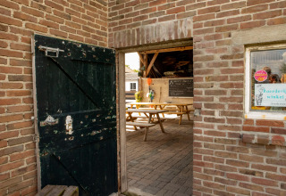 Entrada con puerta de madera abierta, bancos y pizarra en Feather Down Hoeve de Betuwe, Gelderland, Países Bajos.
